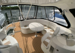 Curved white sofa seating around a round table on a yacht deck with teak flooring and water in the background