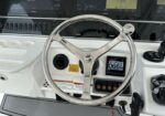 Chrome steering wheel at a boat helm with Garmin navigation screens and control panel behind it, conveying the cockpit setup for navigation and steering.