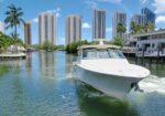 White motor yacht cruising along a canal with high-rise buildings and palm trees in the background on a sunny day