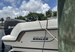 White Boston Whaler boat at a dock, Mercury engine cover visible in background and blue sky with clouds behind palm trees