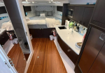 Lux yacht interior: galley on the right with sink and appliances, and a bed area at the rear with cushions on a wood floor.