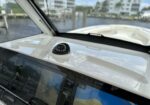 Close-up of a boat helm with a black compass mounted on a white dashboard, flanked by Garmin navigation screens and a view of water and buildings ahead.