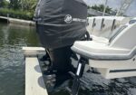 White boat on a lift with a large Mercury outboard motor covered by a dark cover at a dock/boating dock scene (calm water in background).