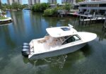 White motorboat with three Yamaha outboard engines docked in a canal by residential buildings; blue sky and greenery reflect on the water.