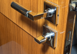 Close-up of a modern chrome door handle and lock on a wooden door.