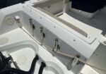 White boat cockpit with five stainless rod holders along the gunwale and a beige power cord plugged into a round outlet on the side.