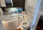 Compact bathroom on a boat or RV with curved white vanity, sink, mirror cabinet, toiletries, washing machine, and toilet.