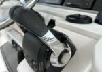 Boat throttle lever with black grip and chrome trim in a white helm console, steering wheel and control gauges visible in the background