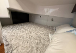Compact ship cabin with a low bed, patterned quilt, and white pillows along a glossy white wall with storage cabinets nearby
