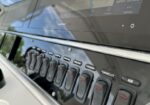 Close-up of a boat helm with a Garmin marine display and a row of labeled rocker switches below, including AUX and LIVEWELL LT under the screen.