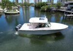 White Grady-White cabin boat with twin Yamaha outboard motors cruising through a calm canal lined with palm trees and waterfront homes.