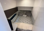 Compact boat cabin with a V-shaped bed, white walls, and wood flooring under soft ceiling lights.