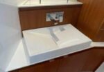 White rectangular bathroom sink basin set into a wooden vanity with a chrome faucet and mirror above; a clean, built-in look.