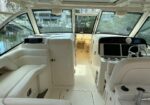 Interior of a luxury white yacht cockpit with helm, two large navigation screens, and a chrome steering wheel, facing a doorway to the cabin.