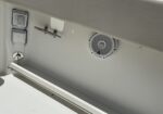 White boat interior wall with a round speaker, two square access panels, and a metal grab bar.