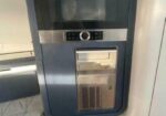 Stainless steel espresso machine with a circular control dial, digital display, and pull-out tray underneath.