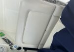 White leather boat seat with a backrest and fold-down cushion, adjacent to a blue fabric cover in a small cabin area.