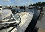 White motorboat docked at a marina with calm water and other boats in the background.