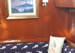 Cozy brown-walled seating area with navy cushions featuring white seahorses and a white fish-patterned pillow. A framed landscape painting and a wall lamp are above.