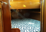 Wood-paneled interior with a curved wooden frame; blue-and-white rope-patterned carpet covers the floor under a low shelf or bed area in a cabin.