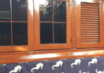 Close-up of a brown wooden cabinet with glass window panels and a slatted door, resting on a dark tablecloth with white seahorse patterns.