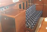 Wood-paneled boat cabin with a navy patterned bench seat along the wall and a small fridge to the left.