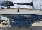 Sailboat on a dry dock with its blue hull peeling and supported by stands.