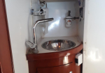 Small boat galley sink with a curved chrome faucet and round stainless basin set in a wooden cabinet.