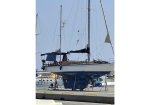 Sailboat on a dry dock with its hull raised, covered in a blue tarp, masts and rigging visible in a marina yard.