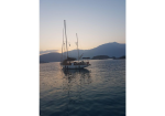 Sailboat anchored on tranquil sea at sunset with mountains in the distance, calm water reflecting the sky edge-to-edge.