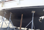 Boat hull resting on keel supports in a dry dock, with a dark bottom and white upper hull.