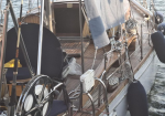Deck of a wooden sailboat with steering wheel, rigging, and life jackets stowed along the railings