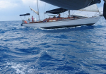 Sailing yacht with people on deck gliding over blue waves under a cloudy sky; white hull with the name ETRADA visible.