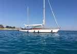 White sailing yacht anchored in calm blue water near a rocky coastline under a clear sky.