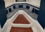 A U-shaped seating area with gray cushions along the boat interior, surrounding a wooden deck and white fiberglass structure.