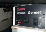 Front panel of an Oman Marine genset control box showing Start/Stop switch, hours meter, and emergency stop in a dim workshop setting.