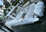 White sport yacht docked at a marina, with a large helm area and white radar domes atop the cabin. One large outboard motor is mounted at the stern.
