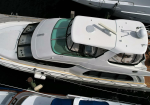 Top-down view of a white luxury motor yacht docked at a marina, showing the cockpit, cabin windows, and teak aft deck beside other boats.