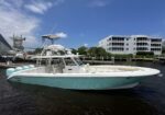 White and teal luxury motorboat docked at a marina with modern apartments in the background, blue sky overhead.