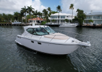 White motor yacht on calm water with waterfront houses and palm trees in the background