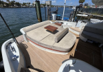 Curved beige-cushioned lounge on a motor yacht deck with a small wooden table, at a marina.