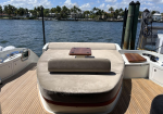Sun loungers on a boat deck with beige cushions and a small wooden table, overlooking a waterway and palm trees.