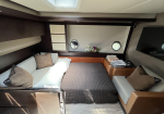 Cozy yacht cabin with a large bed, gray quilt, brown and beige throw pillows, and wood-paneled walls with two round portholes.