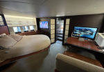 Luxurious yacht cabin with a large round bed, cream bedding, and built-in seating by windows with blinds; a TV is mounted on the opposite wall.