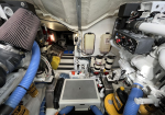 Cramped boat engine room with blue hoses, air filter, yellow oil cans, and electrical panels.