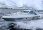 White luxury yacht speeding across choppy water with city skyline in the background.