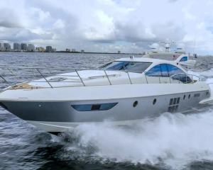 White luxury yacht speeding across choppy water with city skyline in the background.