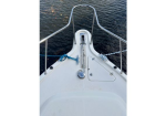 Bow of a white sailboat with stainless steel rails, anchor chain in hawsepipe, and a deck hatch; calm water in the background.
