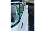 White motorboat moored at a wooden dock, showing the side deck, stainless railing, and cabin window reflecting water.
