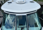 White boat helm with a Garmin radar dome on top, large windshield with dual wipers, dock and water visible in background.